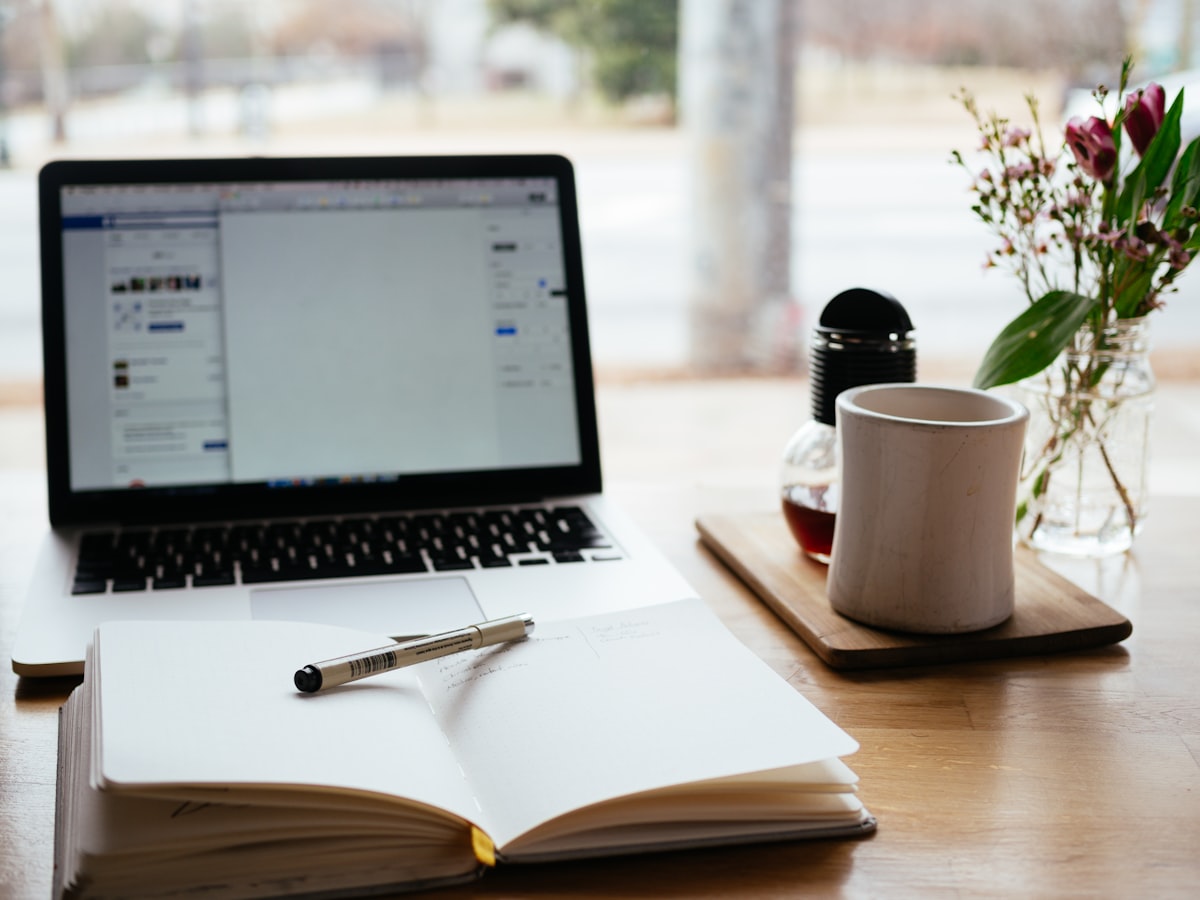 Open notebook with pen, laptop, and coffee on a desk