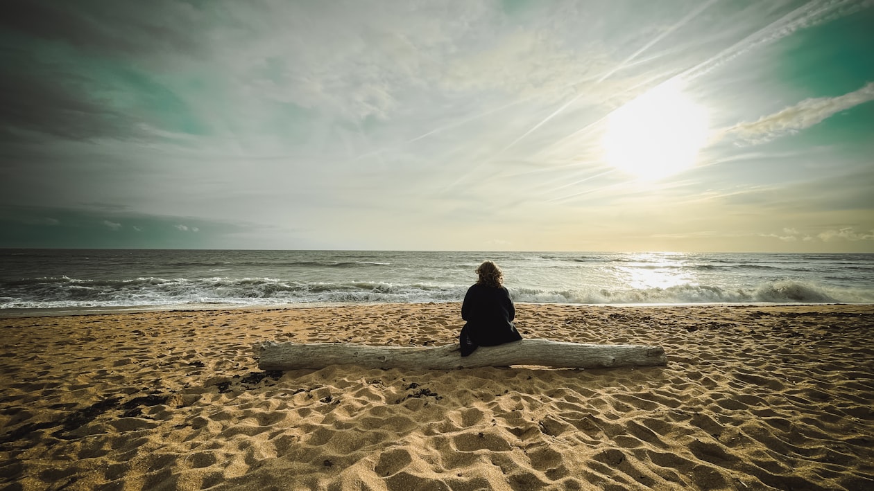 Person sitting on a log facing the ocean contemplating readiness