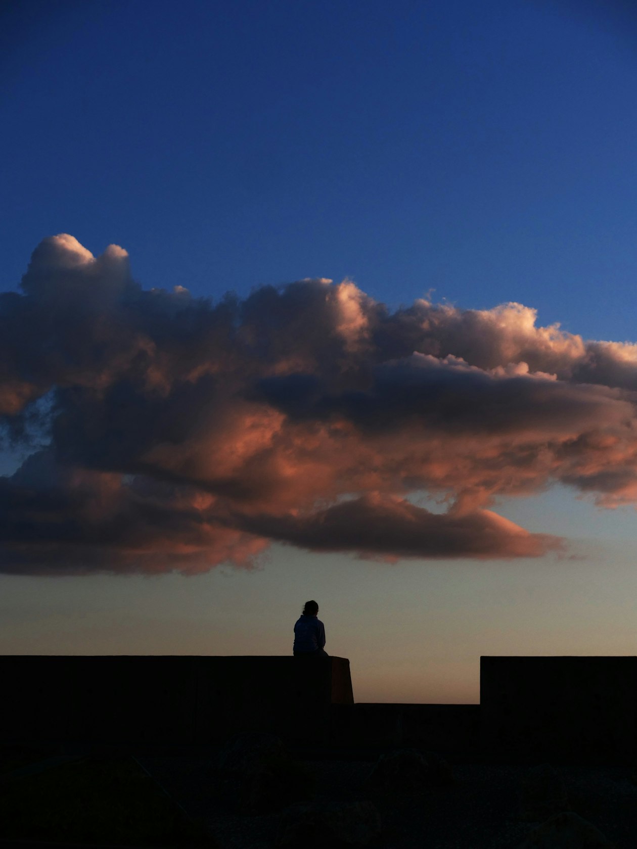 Lone silhouette gazing at dramatic sunset clouds representing quiet readiness