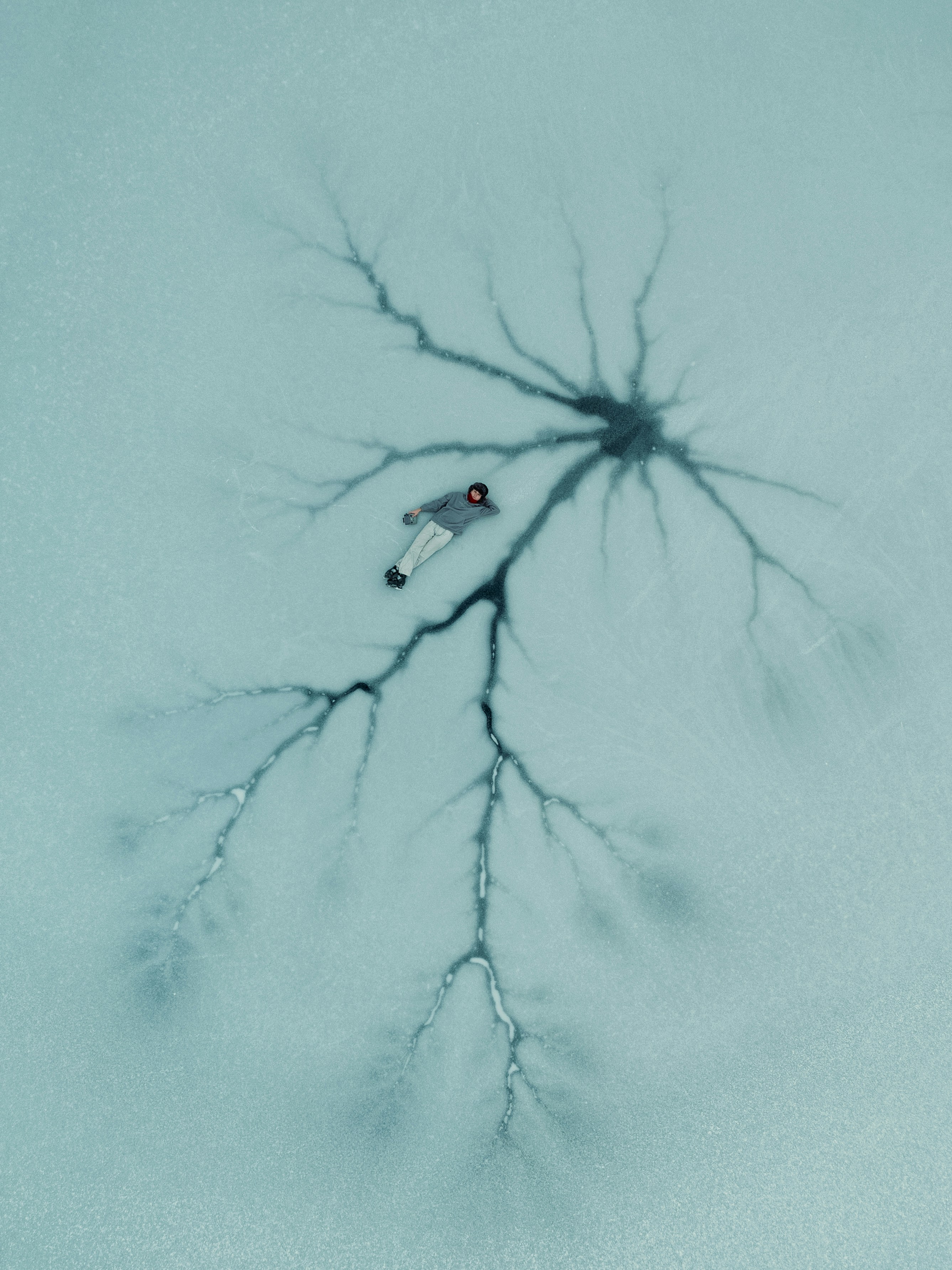 Aerial view of person lying on cracked ice resembling neural networks