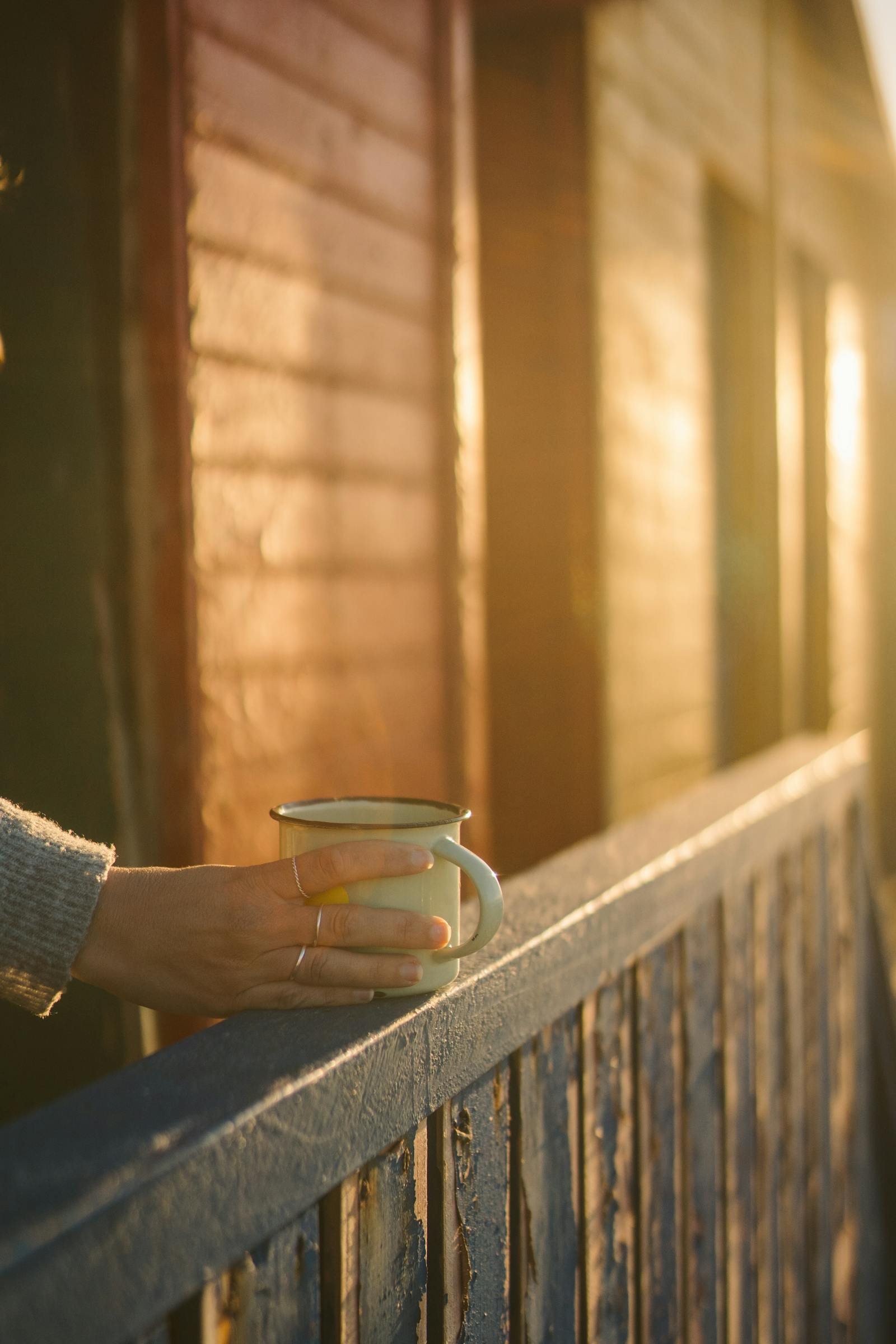 Hand holding a warm enamel mug at golden hour on a wooden railing, evoking morning reflection on the variables of a ceremony