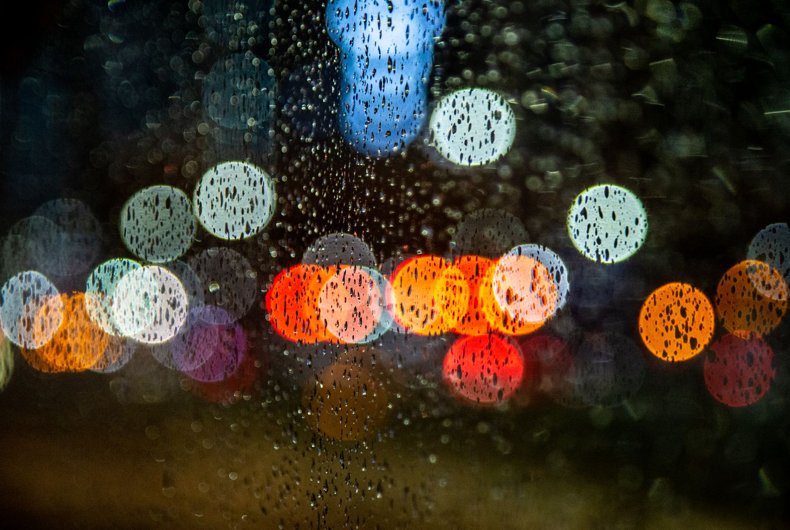 Raindrops on a window at night with soft, colorful city lights blurred behind the glass