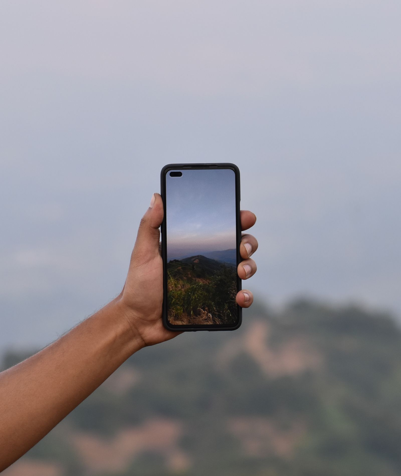 A hand holding up a smartphone that frames the mountain landscape behind it